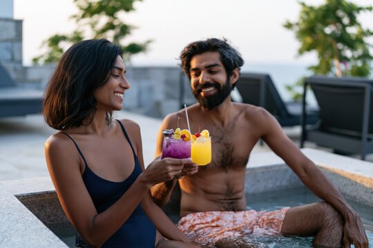 Smiling couple in a poolside hot tub clinking colorful cocktails for summer vacation relaxation and resort spa banner use