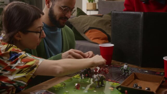 Close up shot of cheerful biracial man throwing dice and moving his figure while playing RPG tabletop game with friends at home