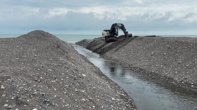 An excavator digs a channel to drain rainwater into the sea.