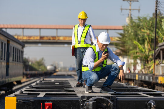 Professional engineer and foreman worker inspecting freight train cargo on railway tracks, Railway technicians working on freight train communicating by radio during cargo train inspection