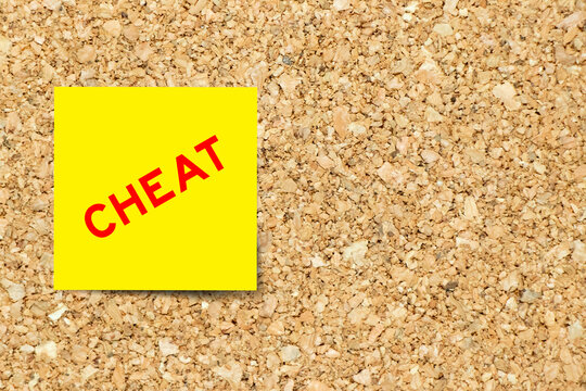 Yellow note paper with word cheat on cork board background with copy space
