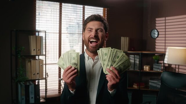 Funny Caucasian middle-aged business man holding fans of money cash dollars yelling shouting laughing loud celebrating happy in office adult 40s businessman male laugh ecstatic yell shout wealthy