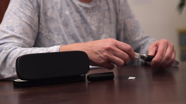 Woman at table assembles medication in medical injection pen, closeup