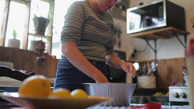 Teen girl kneads dough in kitchen table bowl: Home baking preparation