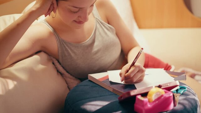Happy and focused high school student smiling while creating secret notes and crib sheets from her phone to cheat on a future test, sitting on a couch with scissors and tape at home.