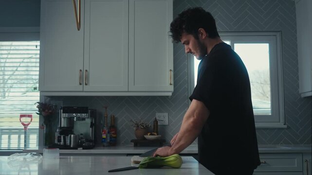 Young man chopping bok choy on white kitchen counter by window on winter day