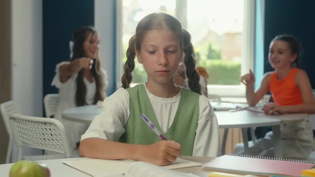 Caucasian teen schoolgirl writing study ignoring teasing laughing classmates schoolchildren in class lesson school daughter child kid girl write studying ignore education bullying psychological trauma