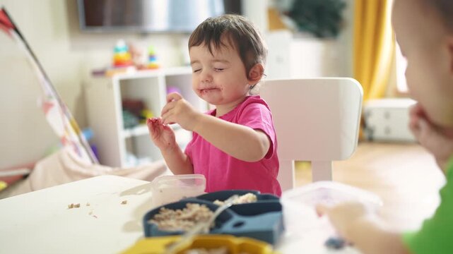 grimy baby eats at the table. baby learns to eat develops fine motor skills gets his face dirty. happy lifestyle family kid dream concept. baby blond daughter eats dirty