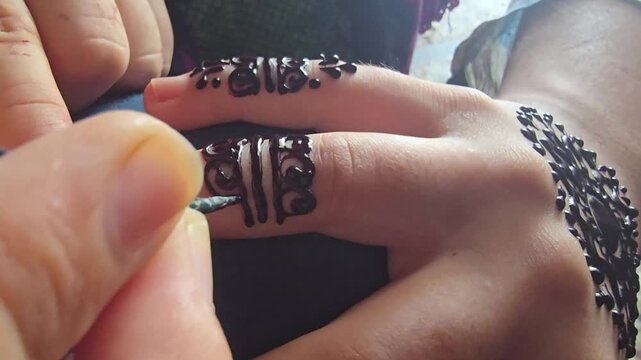 Traditional henna tattoo application on hand, intricate black mehendi floral pattern being drawn on fingers, ethnic body art process for wedding