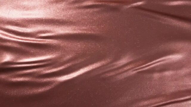 Fabric texture of rich rose gold silk waves gently in soft light to create a luxurious and elegant backdrop for premium design projects.