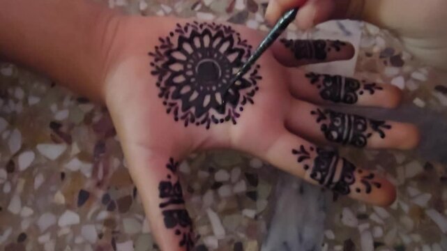 Traditional henna tattoo application on palm, intricate mandala mehndi design, cultural body art process with black ink and applicator tool