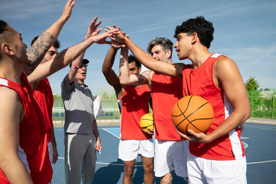 Basketball team and coach forming a huddle, hands together for teamwork