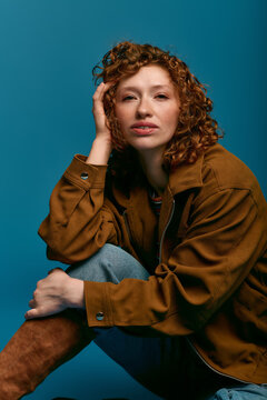 Stylish young woman with curly hair poses confidently against a vibrant blue background