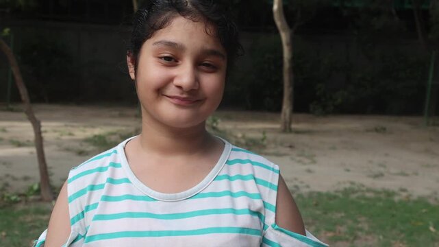  Portrait of a happy young Indian girl smiling and looking at the camera outdoors during evening time. Concept of childhood, innocence, rural lifestyle, happiness, and village life in Indi