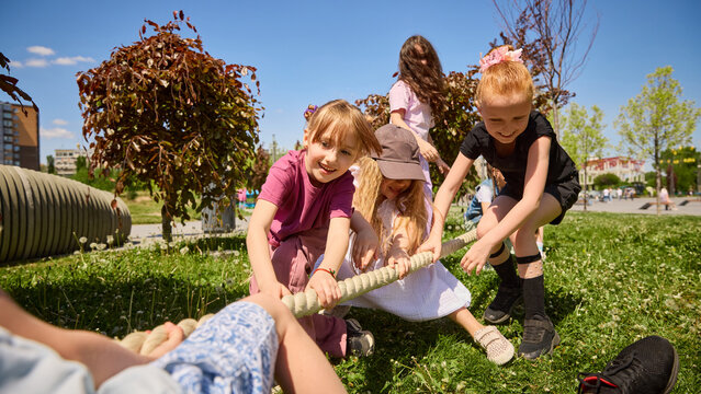 Young children pulling rope in outdoor tug of war game. Concept of playful competition, teamwork, active kids, summer camp activities, school sports, friendship and childcare advertising.