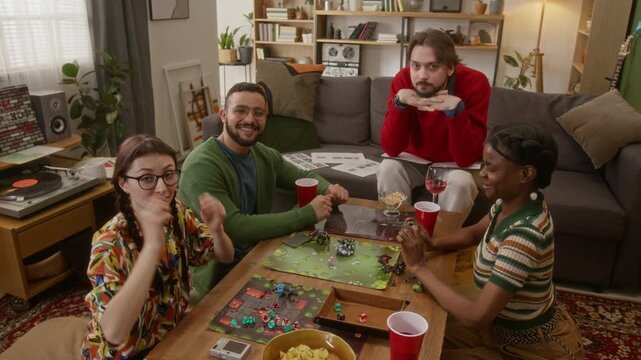High angle group portrait shot of four friends posing for camera while playing tabletop RPG game in cozy living room