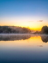 Obraz premium Serene Sunrise Over Misty Lake Reflecting Golden Sky.