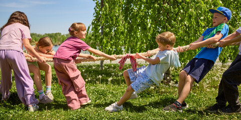 Kids competing in tug of war game near trees and river. Concept of children cooperation, social...