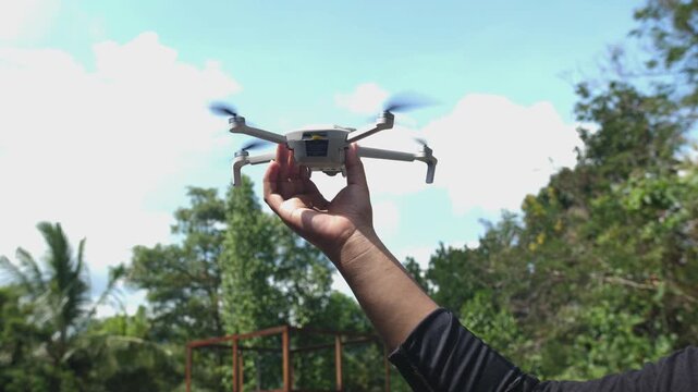 Man releasing a small white quadcopter drone from his hand for takeoff in a sunny outdoor park.
