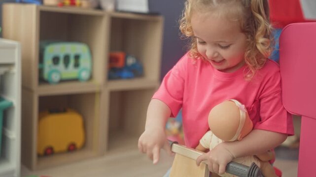 Girl holding doll and gripping wooden ride toy handlebar beside shelves with a toy bus in a playroom building; playful joy.