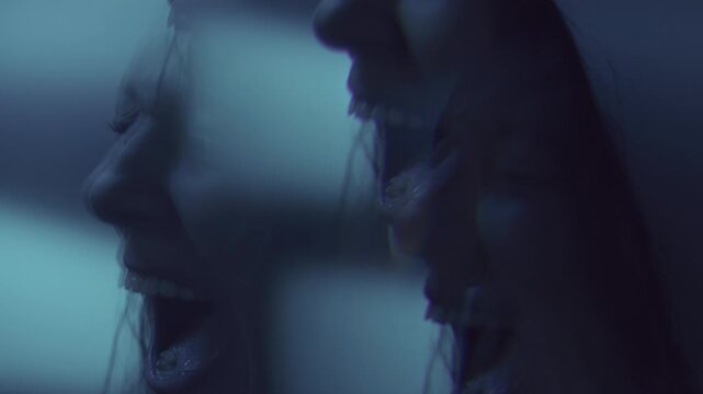Multiple exposure profile portrait of young woman screaming with her mouth wide open in intense emotional pain under dark blue lighting
