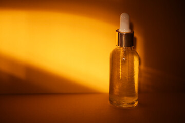Naklejka premium Clear glass dropper bottle with white pipette cap filled with liquid, illuminated by warm golden light against a smooth orange background