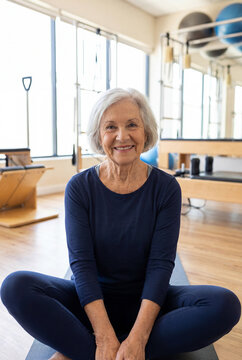 An elderly woman practices yoga in a cozy room, looks into the camera, and smiles