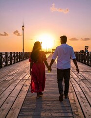Fototapeta premium Couple walking hand in hand on a wooden pier at sunset.