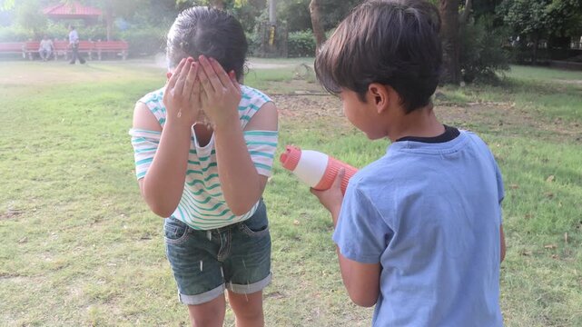 Cute Indian children cooling off during extreme summer heat as a young boy splashes water on a girl&rsquo;s face outdoors in a park, capturing playful childhood moments in hot weather.