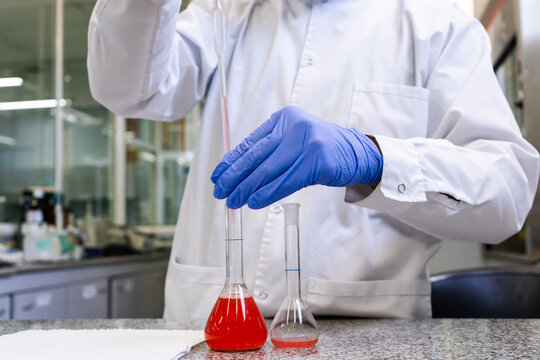 Scientist hands in gloves using pipette with red liquid in volumetric flask in pharmaceutical laboratory