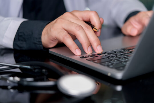 Telemedicine concept doctor typing laptop stethoscope glass desk. Healthcare IT system medical consultation online network expert physician digital workflow health informatics.