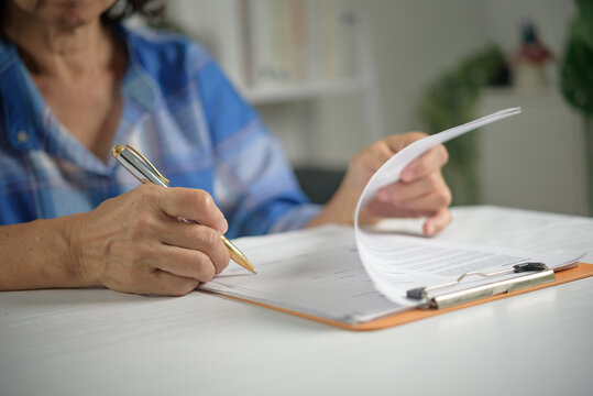 Elderly lifestyle concept showing older person writing on paper form evaluating medical insurance claim managing personal finance and signing testament will at home desk
