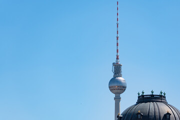 The Berlin TV Tower rises behind the dark dome of Berlin Cathedral under a clear blue sky. This cityscape links modern landmarks with historic architecture. © Jakob