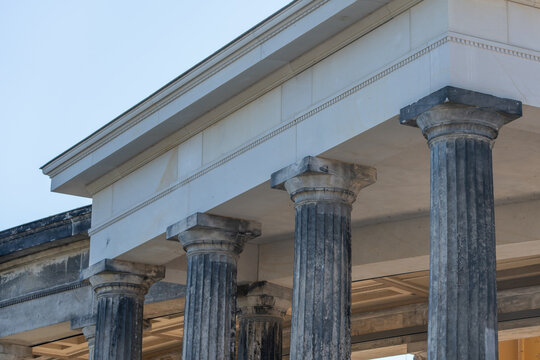 Weathered stone columns support a neoclassical portico on Museum Island in Berlin. The close view highlights fluted pillars, capitals and architectural texture.