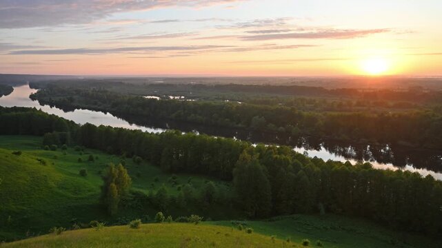 A breathtaking landscape with a winding river flowing through a dense forest and rolling green hills bathed in the warm golden light of the rising sun.
