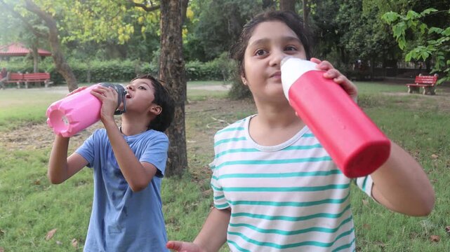 Description: Two Indian children drinking water from bottles outdoors during a very hot summer day in India. Cute kids staying hydrated and cooling themselves in warm sunny weather.