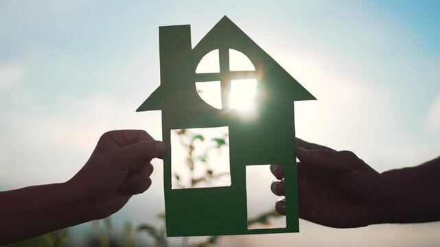 Family mortgage concept. Family holds paper house with their hands at sunset. Family house on loan. Paper house is symbol of family happiness.Housing and mortgage crisis.Dream concept of buying house