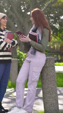 Vertical video: Approaching friend redhead showing phone holding notes walking together on campus