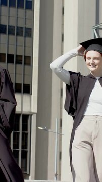 Vertical video: Walking three grads in gowns on campus third grad touching, tossing cap celebrating