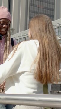 Vertical video: Coming woman in pink hat initiating greeting, hugging friend in white top at stairs