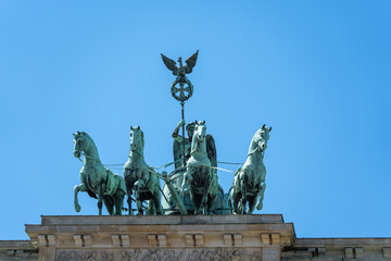 Obraz premium The Brandenburg Gate Quadriga shows horse and eagle sculptures against a clear sky. Bronze patina and stone reliefs highlight Berlin history.