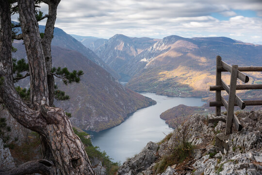 Artificial lake Perucac surrounded with mountains during cloudy day, view point Banjska stena on Tara mountain framed with tree and wooden fence