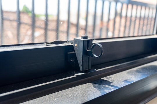 Close-up of a black aluminum window latch lock mechanism installed on a sliding glass window frame, showcasing home security details and interior hardware.