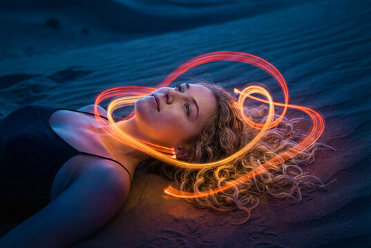 Woman laying on sand at night with orange light swirl
