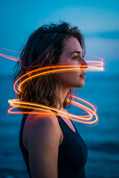 Woman in profile at night with an orange light swirl by the ocean