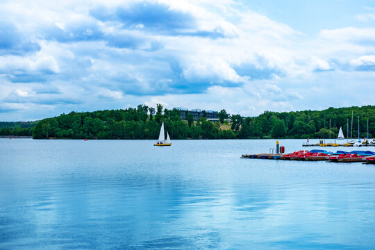 Family riding red pedal boat on Bostalsee lake marina full sailboats, lake with sailboats, cloudy sky, summer day reservoir, sailing school, water sports, peaceful nature beautiful European in summer