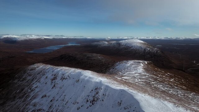 Drone flyover of snow covered ridge and Highland loch