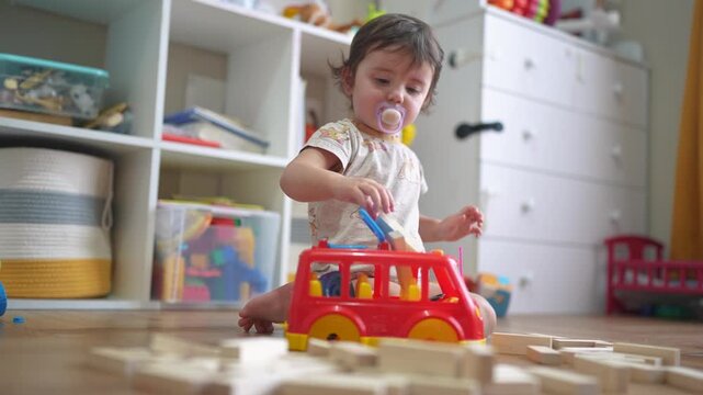 baby plays with a toy bus and puts wooden sticks in the hatch. development of fine motor skills concept. baby learns to put sticks toys into a bus car indoors in kindergarten lifestyle