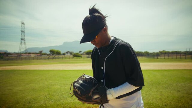 A focused baseball pitcher stands on the mound, preparing to throw the ball. She adjusts her grip, observing the field with concentration.