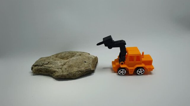 Stop motion of orange toy excavator breaking a large rock with its hydraulic jack hammer on a white background. Construction and demolition concept for creative projects.
